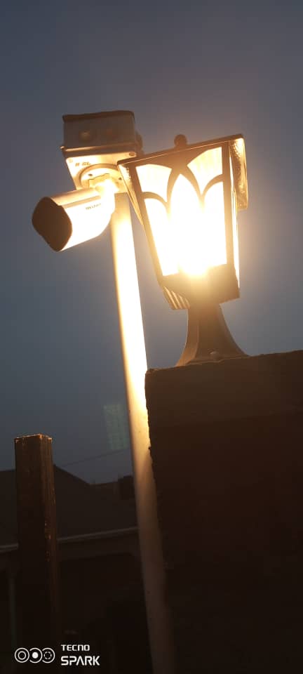 CCTV bullet camera mounted on a pole at dusk beside a street lamp